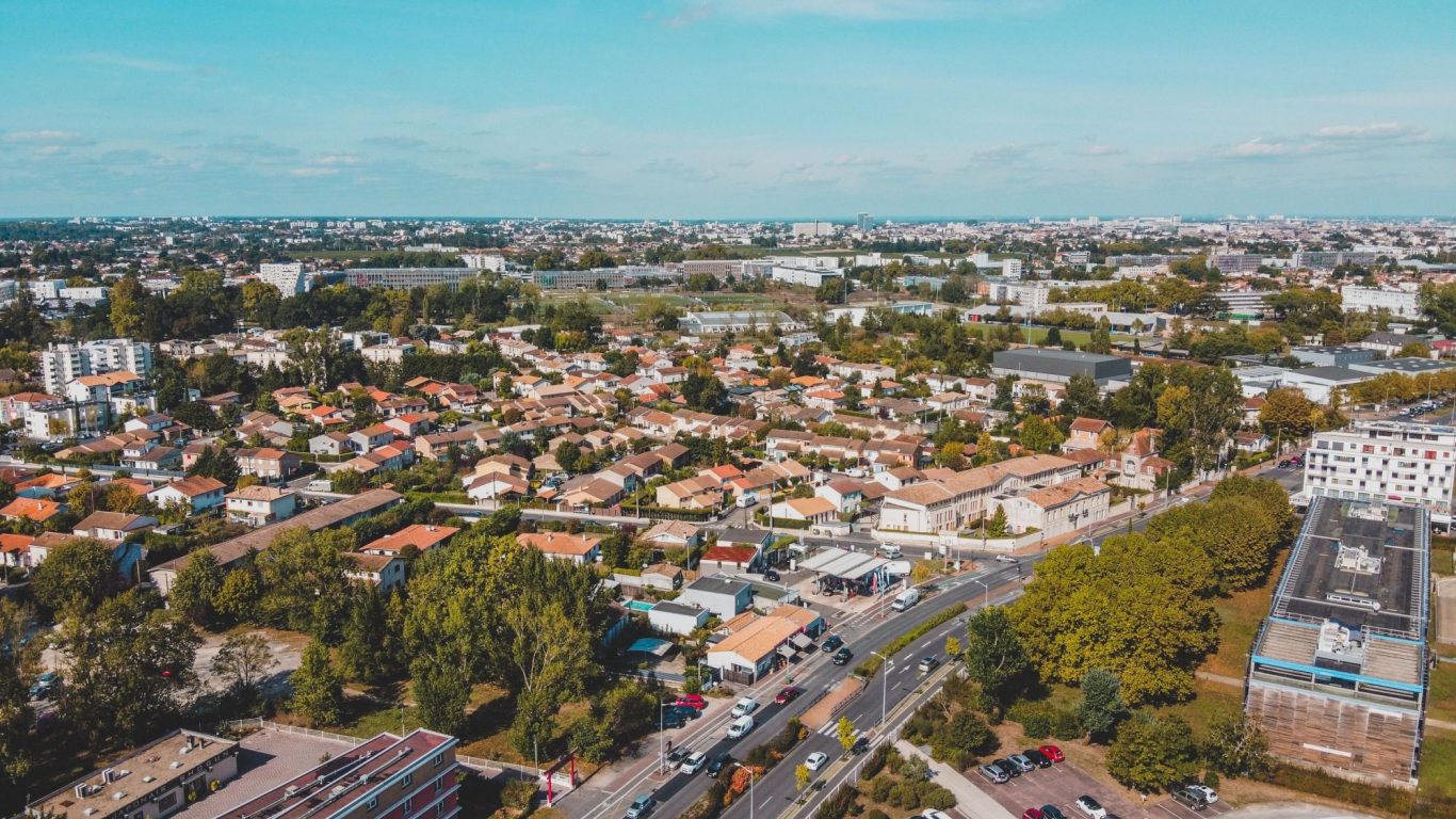 Vue aérienne d'un quartier résidentiel avec maisons et routes, sous un ciel bleu.