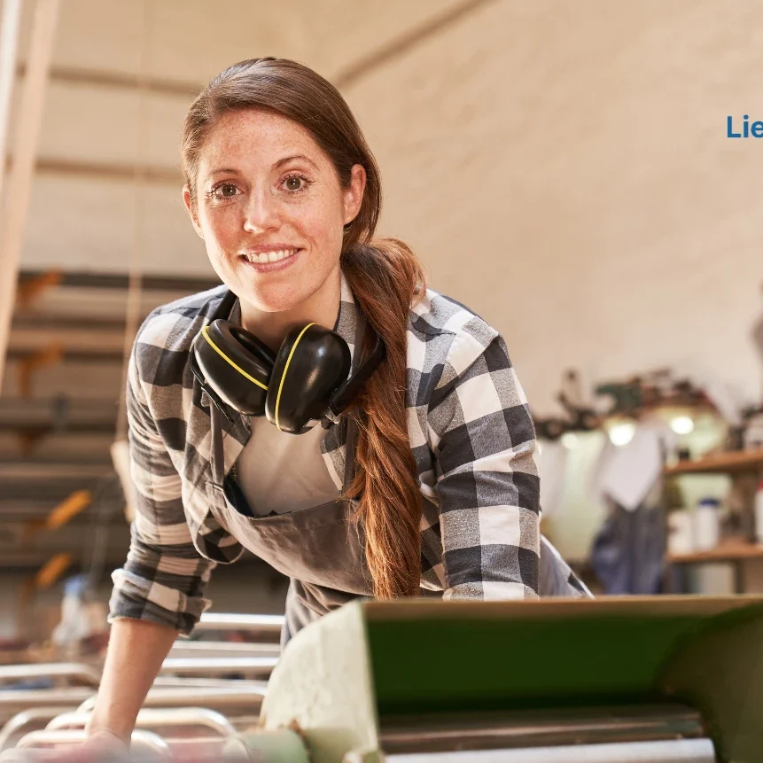 Femme en tenue de travail, souriant, avec des écouteurs, dans un atelier.