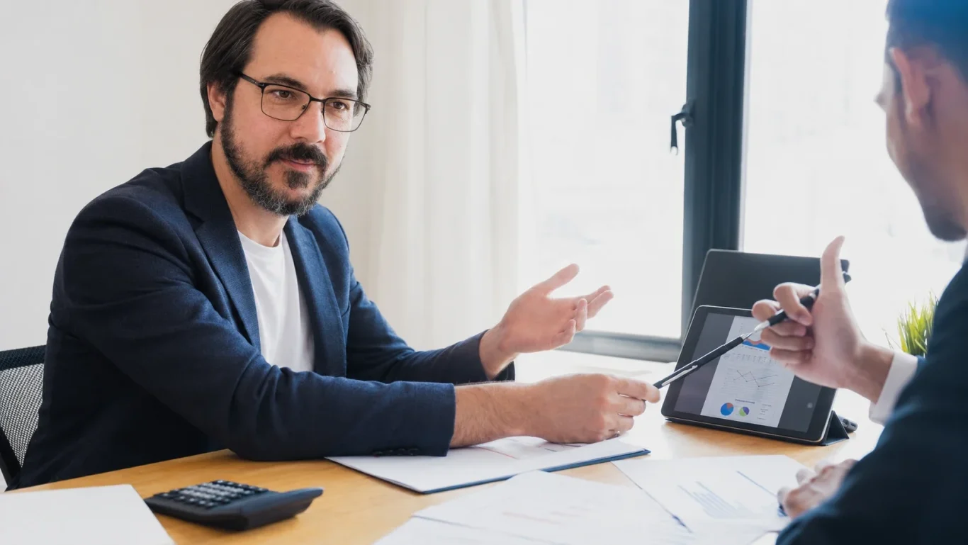 Un homme en costume discute avec un collègue dans un bureau lumineux.